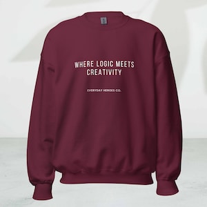 May include: A maroon crewneck sweatshirt with the text "WHERE LOGIC MEETS CREATIVITY" and "EVERYDAY HEROES CO." printed in white. The sweatshirt has long sleeves and ribbed cuffs and hem.