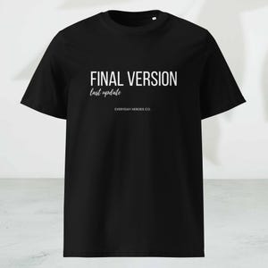 以下が含まれることがあります： 黒いTシャツ。白い文字で「FINAL VERSION」と書かれ、その下に「last update」と書かれています。「EVERYDAY HEROES CO.」の文字が下にあります。シンプルでミニマルなデザイン。