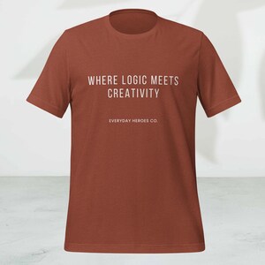 May include: A rust-colored t-shirt with the text "WHERE LOGIC MEETS CREATIVITY" in white, along with "EVERYDAY HEROES CO." below. The short-sleeved shirt is made of a soft material.