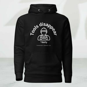 May include: Black hooded sweatshirt with a front pocket and white graphic. The graphic reads "Tools disappear *daily" around an outline of a construction worker. The text "EVERYDAY HEROES CO." is below the graphic.