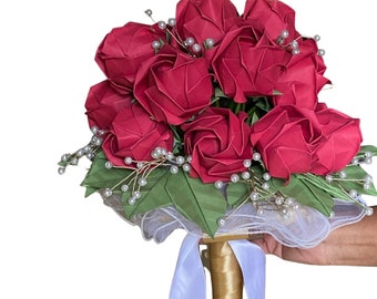 May include: A bouquet of red origami roses with pearl accents and green leaves, tied with a white ribbon and a gold handle.