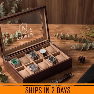 May include: A dark brown wooden watch box with a glass lid featuring a white engraved shield, the letter A, and the name ANDREW. The interior is lined with beige fabric and contains four wristwatches and several empty cushioned slots.