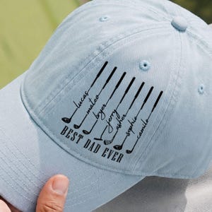 May include: Light blue baseball cap with the text "BEST DAD EVER" and names of children. The cap features black golf club graphics. A perfect gift for a golf-loving dad.