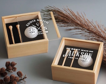 May include: Two square wooden gift boxes with sliding clear lids, each containing a white golf ball and two wooden tees. The first box features the text Eddie Smith, EST 2022, and the second box features the text Best Man, Jackson, Feb. 12, 2025.