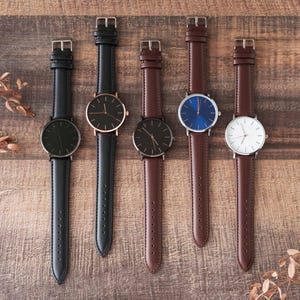 four watches are lined up on a wooden surface