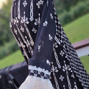 May include: A black and white embroidered dress with a lace trim on the sleeves. The dress has a geometric pattern and floral motifs.