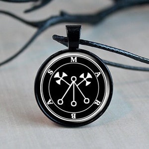 May include: A black pendant necklace with a silver circle charm featuring a white sigil with the letters "S.A.M.A.B.A." around the edge.