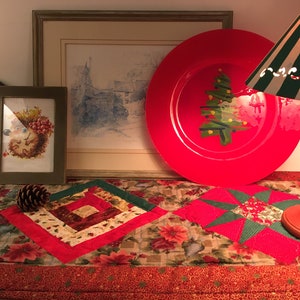 May include: A festive holiday display featuring a red plate with a green Christmas tree graphic, a framed hedgehog illustration, a framed landscape print, a pinecone, and a table runner with poinsettia patterns under a green and white lamp.