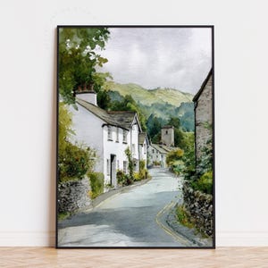 May include: Watercolor painting of a quaint village street with white houses and a church tower. The road curves through the scene, leading towards green hills under a cloudy sky. The artwork is framed in black.