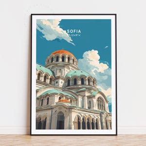 May include: A framed art print featuring a stylized illustration of the Alexander Nevsky Cathedral in Sofia, Bulgaria. The artwork showcases the cathedral's white facade, turquoise domes, and an orange dome against a blue sky with clouds. The text "SOFIA BULGARIA" is at the top.