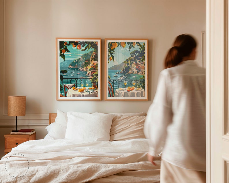 K&ouml;nnte beinhalten: Zwei gerahmte Vintage-Reiseposter mit einer K&uuml;stenlandschaft von Positano und einer Tischdekoration mit Gl&auml;sern und Fr&uuml;chten. Die Poster h&auml;ngen an einer Wand &uuml;ber einem Bett mit wei&szlig;en Bettw&auml;sche und einem braunen Kopfteil.