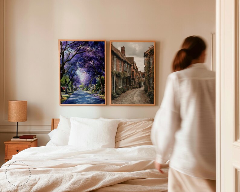 Peut inclure: Deux impressions encadr&eacute;es sont accroch&eacute;es au-dessus d'un lit. L'une repr&eacute;sente une rue bord&eacute;e d'arbres &agrave; fleurs violettes. L'autre montre une rue pav&eacute;e avec des b&acirc;timents en briques. Les deux sont dans des cadres en bois clair.