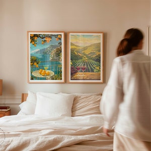 May include: Two framed vintage travel posters, one depicting a coastal scene with a lemon tree and the other showing a vineyard landscape. The posters are hanging on a wall above a bed with white linens.