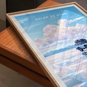 May include: A framed poster with a white car driving on a salt flat with a blue sky and white clouds. The poster says "Salar de Uyuni, Bolivia" in the top left corner.