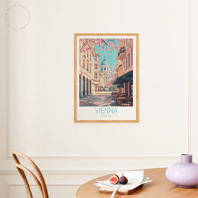 May include: A framed art print depicting a street scene in Vienna, Austria. The print shows a view down a cobbled street towards a domed building. Pink blossoms frame the top of the image, with the words "Vienna" and "Austria" printed at the bottom.