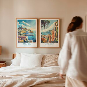 May include: Two framed travel posters on a light beige wall above a bed with white linens. The poster on the left features a colorful illustration of a city with the text "MALTA MEDITERRANEAN" below. The poster on the right features a colorful illustration of a city with the text "MALAGA SPAIN" below.