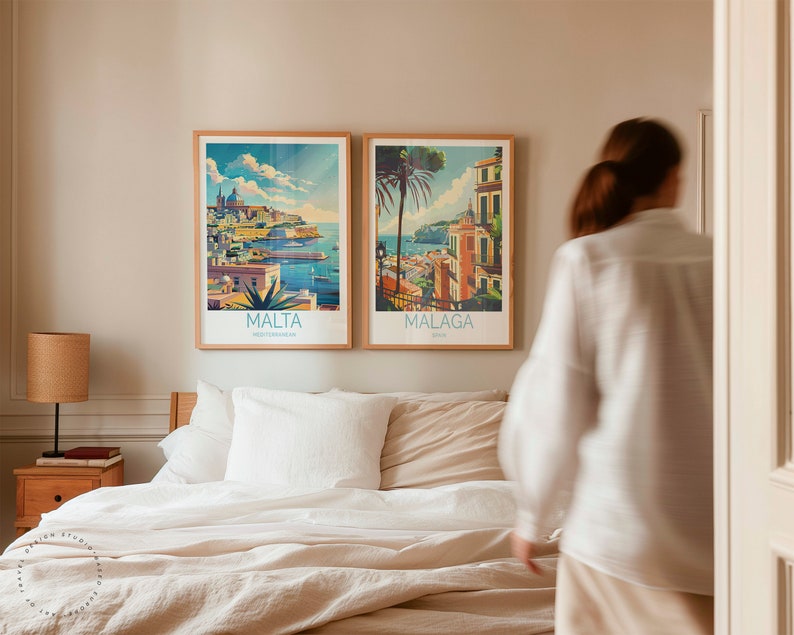 May include: Two framed travel posters on a light beige wall above a bed with white linens. The poster on the left features a colorful illustration of a city with the text "MALTA MEDITERRANEAN" below. The poster on the right features a colorful illustration of a city with the text "MALAGA SPAIN" below.