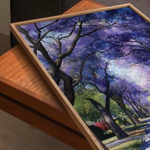 Peut inclure: Une impression encadr&eacute;e d'aquarelle repr&eacute;sentant un paysage avec des arbres aux fleurs violettes. L'&oelig;uvre est encadr&eacute;e dans un cadre en bois clair, montrant une sc&egrave;ne de parc avec un chemin et de la verdure.