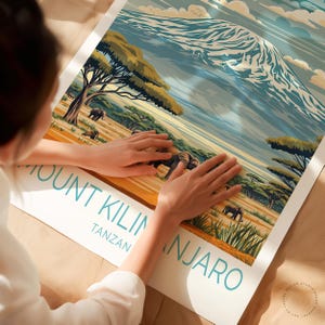May include: A vintage travel poster featuring a scenic view of Mount Kilimanjaro in Tanzania. The poster has a blue, green, and yellow color scheme and depicts a mountain with snow-capped peaks, lush green trees, and elephants in the foreground. The text "Mount Kilimanjaro, Tanzania" is printed in a teal blue font at the bottom of the poster.