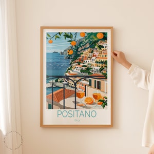 May include: A colorful illustration of Positano, Italy, with a view of the town from a balcony overlooking the Mediterranean Sea. The illustration features a table with two glasses of orange juice and a plate of oranges. The text "Positano, Italy" is printed below the image.