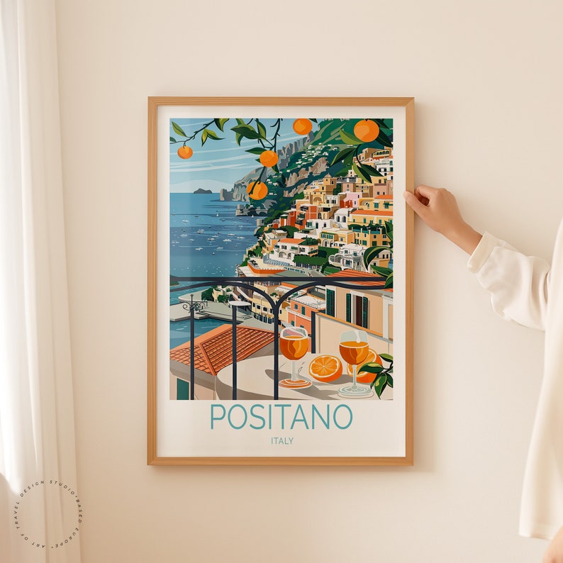 May include: A colorful illustration of Positano, Italy, with a view of the town from a balcony overlooking the Mediterranean Sea. The illustration features a table with two glasses of orange juice and a plate of oranges. The text "Positano, Italy" is printed below the image.