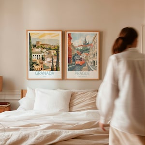 Puede incluir: Dos p&oacute;sters de viaje enmarcados, uno que representa Granada, Espa&ntilde;a, y el otro Praga, Rep&uacute;blica Checa, cuelgan en una pared de color beige claro sobre una cama blanca con un edred&oacute;n de lino beige y almohadas blancas.