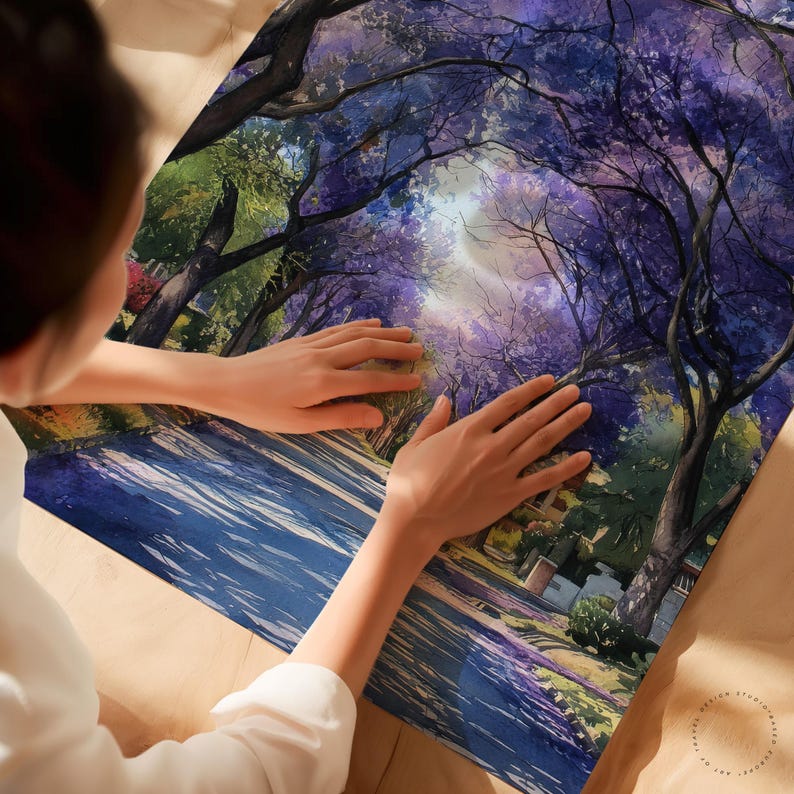 Peut inclure: Une impression aquarelle vibrante d'une rue bord&eacute;e d'arbres aux fleurs violettes. L'&oelig;uvre pr&eacute;sente un ciel lumineux et ensoleill&eacute; per&ccedil;ant &agrave; travers la canop&eacute;e. L'impression est une sc&egrave;ne de paysage avec une route et des b&acirc;timents.