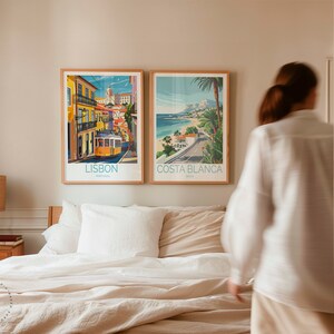 May include: Two framed travel posters on a wall above a bed. The poster on the left is for Lisbon, Portugal and features a yellow tram. The poster on the right is for Costa Blanca, Spain and features a beach scene.