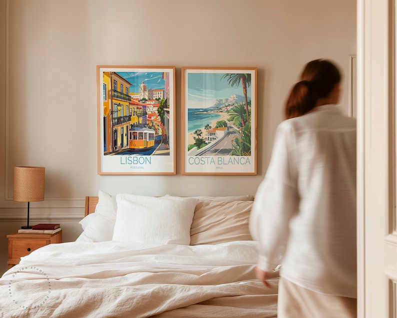 May include: Two framed travel posters on a wall above a bed. The poster on the left is for Lisbon, Portugal and features a yellow tram. The poster on the right is for Costa Blanca, Spain and features a beach scene.