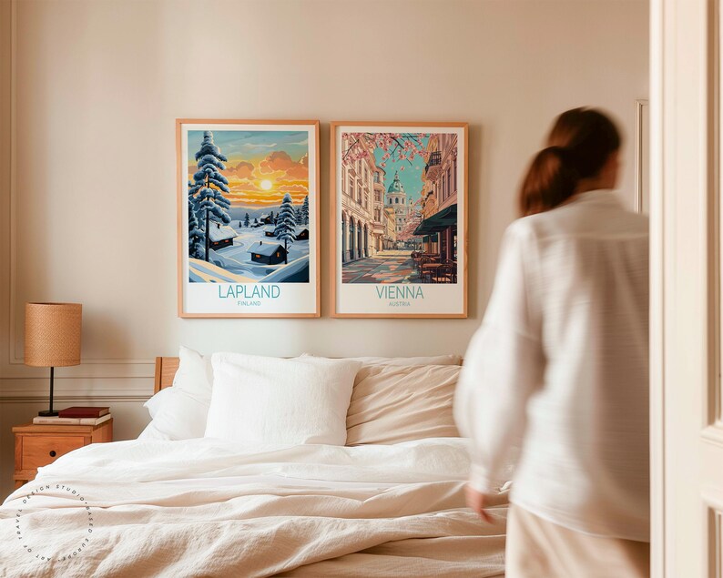 May include: Two framed travel art prints. One shows a winter scene in Lapland, Finland, with snow-covered trees and a sunset. The other depicts a street scene in Vienna, Austria, with buildings and cherry blossoms. Both prints have wooden frames.