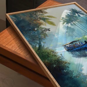 Puede incluir: Pintura a la acuarela de una escena de r&iacute;o tropical con un barco que transporta pasajeros. La obra de arte est&aacute; enmarcada en un marco de madera clara. La pintura presenta exuberante follaje verde, palmeras y un barco azul en el agua.