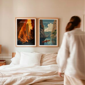 K&ouml;nnte beinhalten: Zwei gerahmte Landschaftskunst-Drucke. Der erste Druck zeigt einen Canyon mit warmen Orange- und Gelbt&ouml;nen und dem Text "CARLSBAD CAVERNS". Der zweite Druck zeigt einen Kajakfahrer auf einem blauen See mit dem Text "CHANNEL ISLANDS". Beide Drucke haben Holzrahmen.