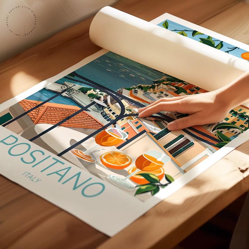 May include: A colorful illustration of Positano, Italy, with a view of the town from a balcony. The illustration features a glass of orange juice and a lemon tree. The text "Positano, Italy" is printed in blue on a white background.