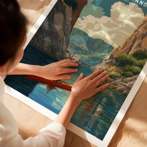 K&ouml;nnte beinhalten: Ein Landschaftsposter mit einer Flusslandschaft, Bergen und einem roten Boot. Das Kunstwerk hat einen Vintage-Reiseplakatstil mit einer blau-braunen Farbpalette. Das Poster wird von einer Person gehalten.