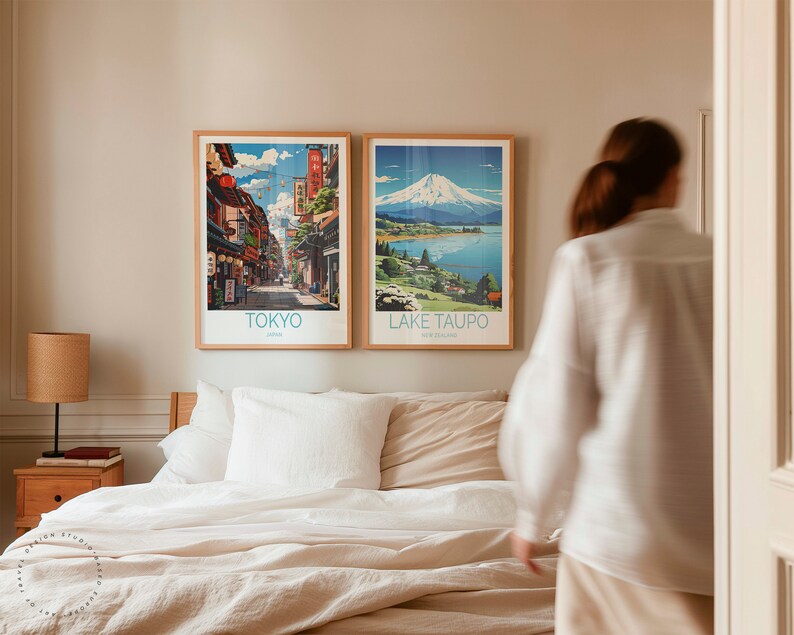 May include: Two framed travel posters on a wall above a bed with white linen. The poster on the left shows a street scene in Tokyo, Japan. The poster on the right shows a mountain and lake scene in Lake Taupo, New Zealand.