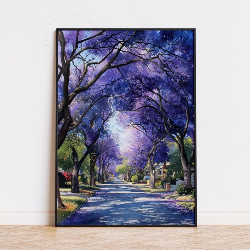 Peut inclure: Une peinture &agrave; l'aquarelle encadr&eacute;e repr&eacute;sente une rue bord&eacute;e d'arbres aux fleurs violettes. L'&oelig;uvre pr&eacute;sente une route menant au loin, avec des maisons visibles. La peinture est dans un cadre noir.
