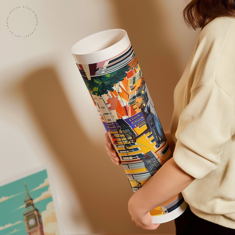May include: A rolled up poster featuring a colorful illustration of a city scene with buildings, streets, and people. The poster is being held by a person's hand.