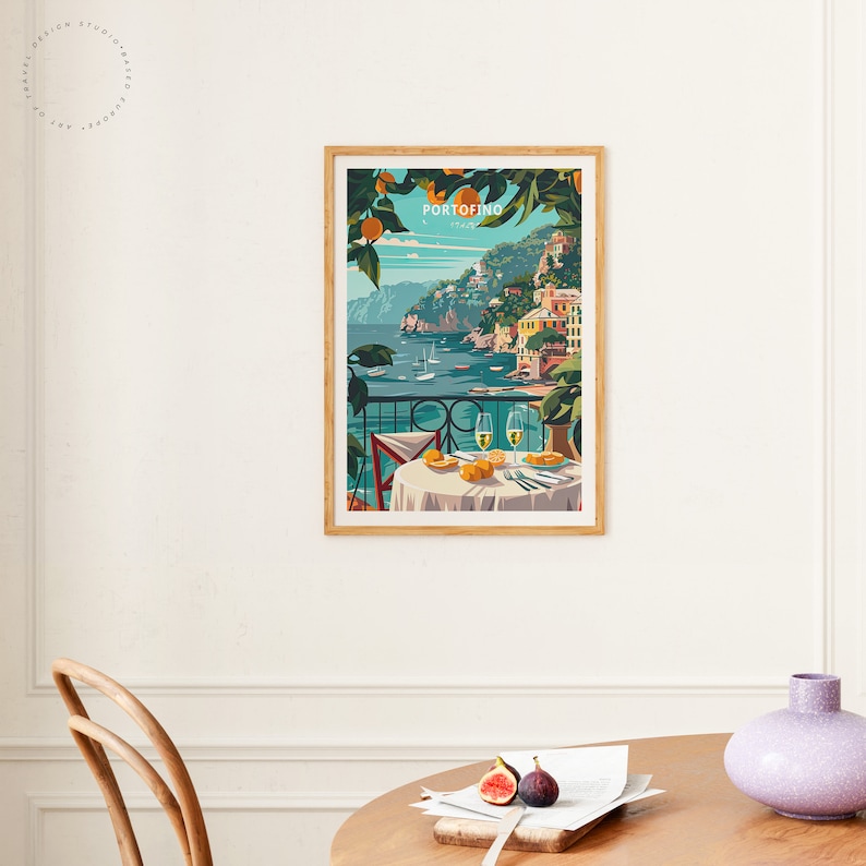 K&ouml;nnte beinhalten: Ein gerahmtes Poster mit einer farbenfrohen Illustration einer K&uuml;stenstadt mit Geb&auml;uden auf einer Klippe mit Blick auf ein blaues Meer. Das Poster tr&auml;gt den Text "PORTOFINO" in einem wei&szlig;en Kasten mit rotem Rand. Das Poster h&auml;ngt an einer wei&szlig;en Wand.
