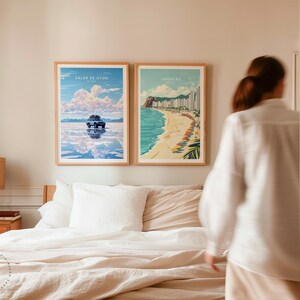 May include: Two framed travel posters hanging on a white wall above a bed with white and beige bedding. The poster on the left shows a car driving on a salt flat with the text "Salar de Uyuni, Bolivia". The poster on the right shows a beach scene with the text "Jaragu&aacute;, Brazil".