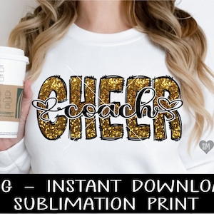 May include: A white t-shirt with a gold glitter design that says "Cheer Coach" with a heart on each side of the word "coach".