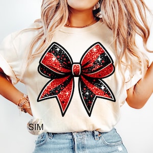 May include: A white t-shirt with a red and black glitter bow design.