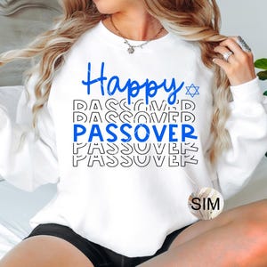 May include: White sweatshirt with the text "Happy Passover" repeated multiple times in blue and black. A blue Star of David is above the text. The sweatshirt has a SIM logo on the bottom right corner.