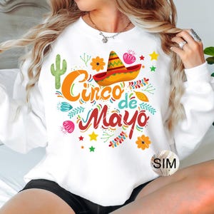May include: White sweatshirt with a colorful graphic design that says "Cinco de Mayo" with a sombrero and cactus.