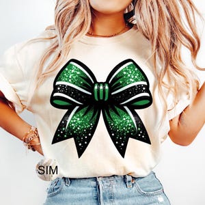 May include: A white t-shirt with a green and black glitter bow design.