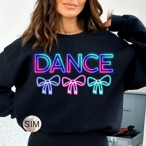 Puede incluir: Sudadera negra con la palabra "DANCE" en azul neón y rosa, con tres gráficos de lazo debajo. La sudadera es de cuello redondo.