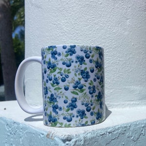 May include: White ceramic mug with a blue and green blueberry pattern.