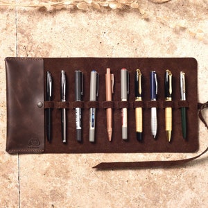 May include: A brown leather pen roll with 10 slots for pens. The roll is unrolled and shows a variety of pens, including black, silver, gold, and copper.