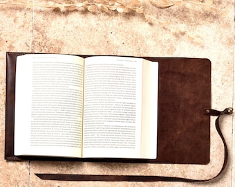 May include: A brown leather book cover with a strap closure. The cover is open to reveal a book with white pages and black text.
