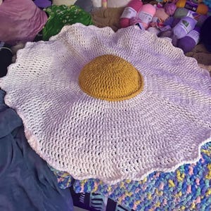 May include: A white crocheted rug shaped like a fried egg with a yellow crocheted yolk in the center.