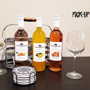 May include: Three bottles of Moira Rose wine, a pink, a yellow, and a peach color, with labels featuring fruit illustrations. The bottles are on a dark wooden table with two wine glasses and a set of coasters.